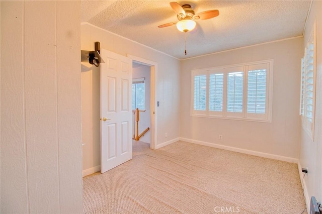 empty room featuring ceiling fan, crown molding, light colored carpet, and a textured ceiling