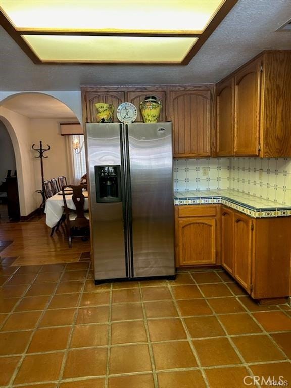 kitchen featuring tile patterned floors, tile counters, stainless steel fridge, and backsplash