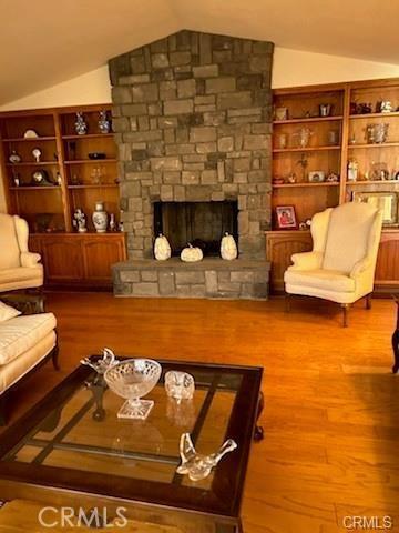 living room featuring built in features, hardwood / wood-style flooring, vaulted ceiling, and a stone fireplace