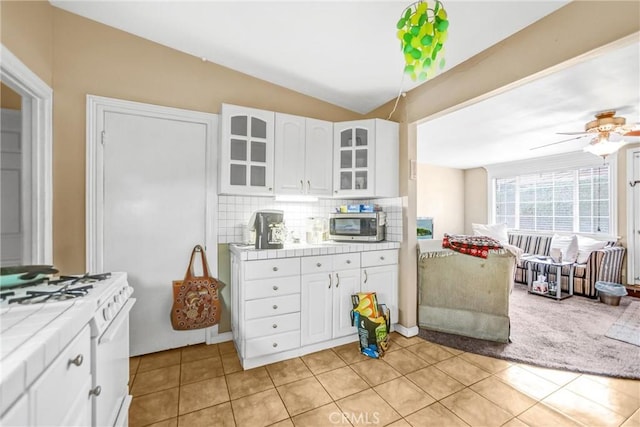 kitchen featuring light tile patterned flooring, white cabinetry, decorative backsplash, tile counters, and gas range gas stove