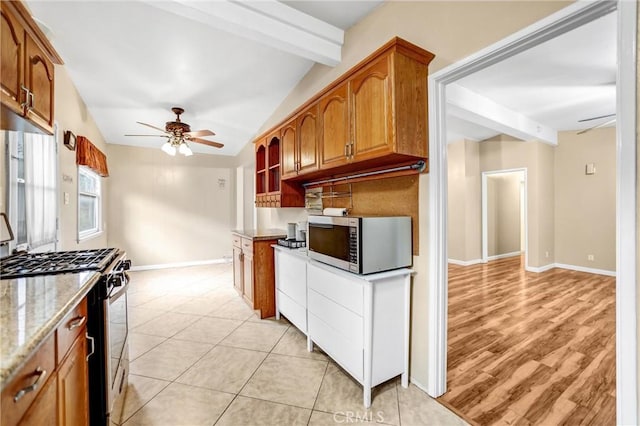 kitchen featuring vaulted ceiling with beams, light stone counters, light tile patterned floors, ceiling fan, and stainless steel appliances