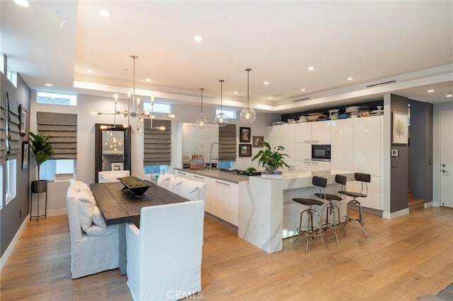 kitchen with black microwave, a spacious island, light hardwood / wood-style flooring, white cabinets, and hanging light fixtures