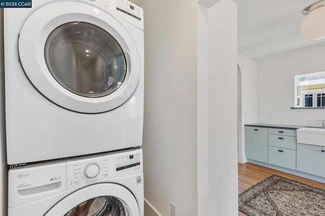 laundry area with stacked washer / dryer, hardwood / wood-style floors, and sink