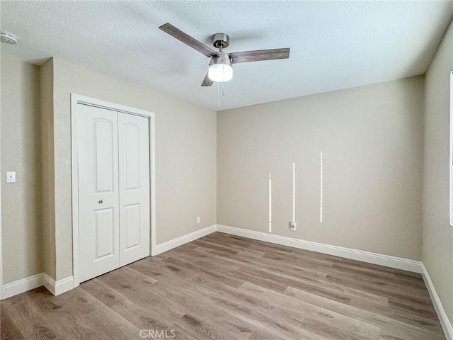 unfurnished bedroom with a textured ceiling, a closet, light hardwood / wood-style flooring, and ceiling fan