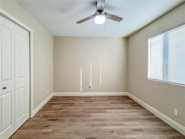 unfurnished bedroom with ceiling fan, a closet, a textured ceiling, and light hardwood / wood-style flooring