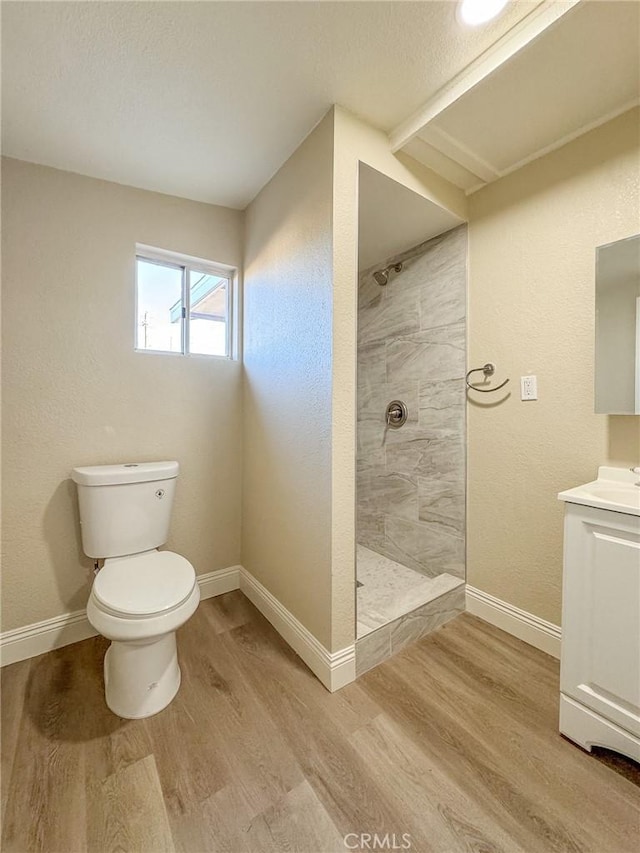 bathroom featuring hardwood / wood-style flooring, vanity, toilet, and a tile shower