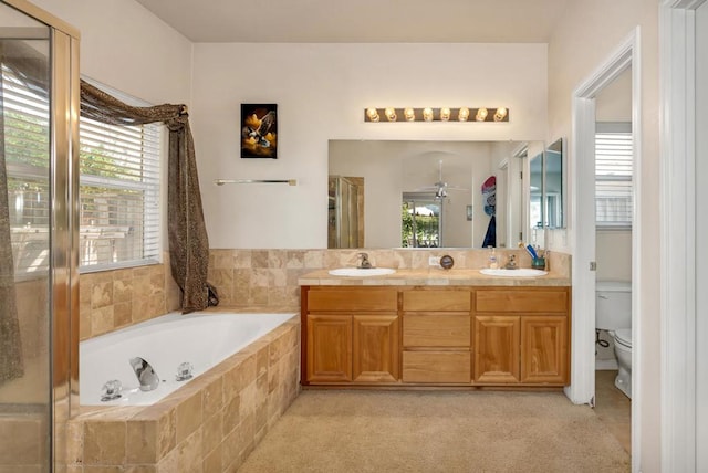 bathroom featuring ceiling fan, tiled tub, toilet, and vanity