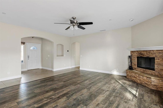 unfurnished living room with hardwood / wood-style floors, a stone fireplace, and ceiling fan