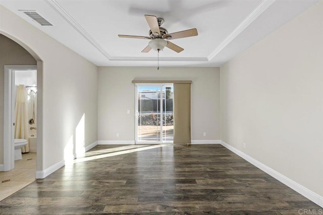 spare room with ornamental molding, a tray ceiling, ceiling fan, and dark wood-type flooring