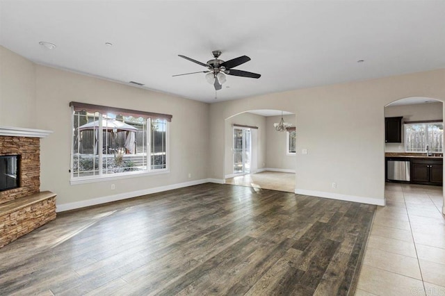 unfurnished living room with ceiling fan with notable chandelier, sink, wood-type flooring, and a fireplace