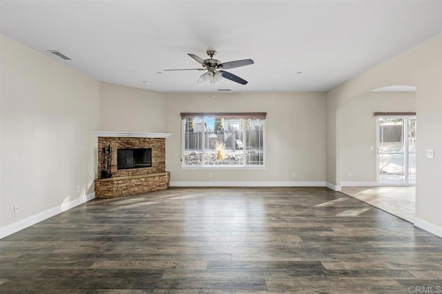 unfurnished living room featuring a stone fireplace, a wealth of natural light, ceiling fan, and dark wood-type flooring