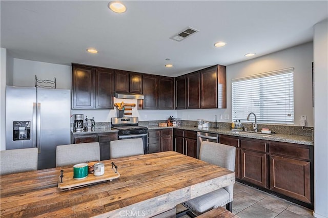 kitchen with dark brown cabinetry, sink, dark stone counters, light tile patterned floors, and stainless steel appliances