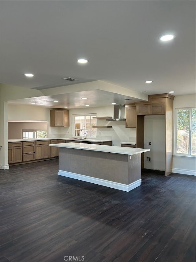 kitchen with wall chimney exhaust hood, a center island, sink, and dark wood-type flooring