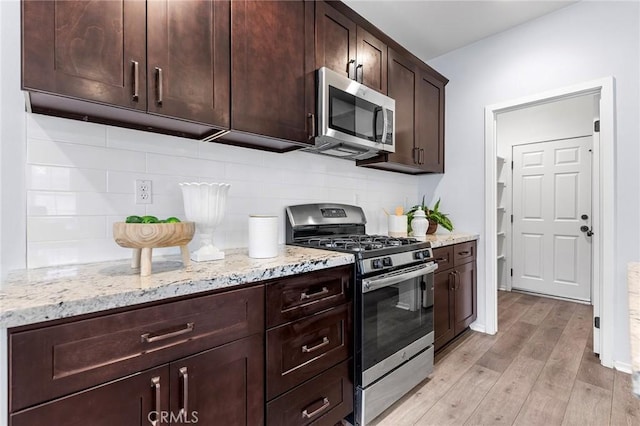 kitchen with decorative backsplash, light stone counters, dark brown cabinets, stainless steel appliances, and light hardwood / wood-style floors