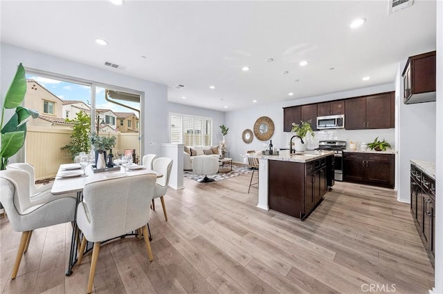 kitchen with sink, stainless steel appliances, a kitchen island with sink, dark brown cabinets, and light wood-type flooring