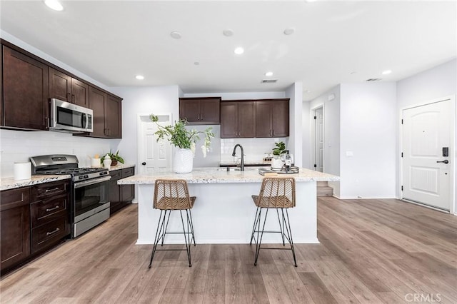 kitchen with a breakfast bar, stainless steel appliances, a center island with sink, and light hardwood / wood-style floors