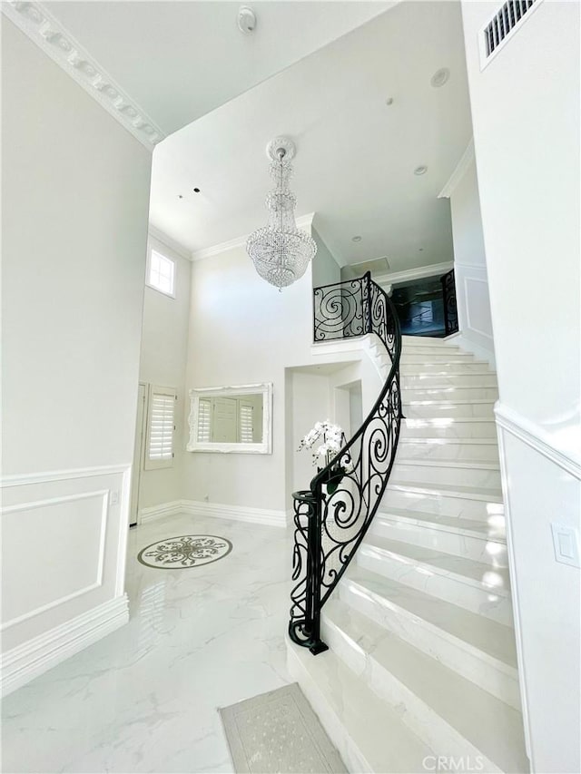 stairway with a towering ceiling, ornamental molding, and an inviting chandelier