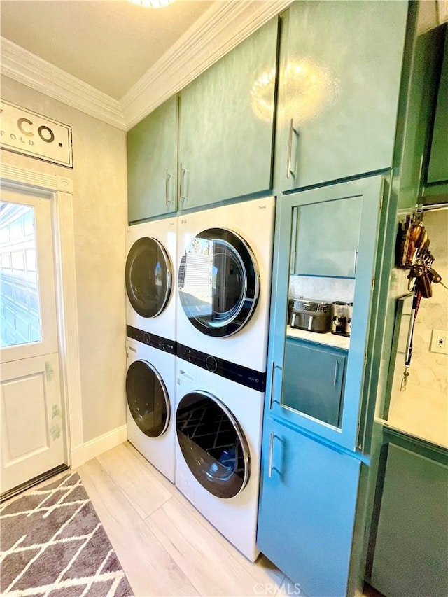 clothes washing area with crown molding, cabinets, and stacked washer and dryer