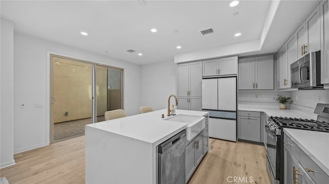 kitchen featuring gray cabinetry, sink, stainless steel appliances, light hardwood / wood-style flooring, and a center island with sink