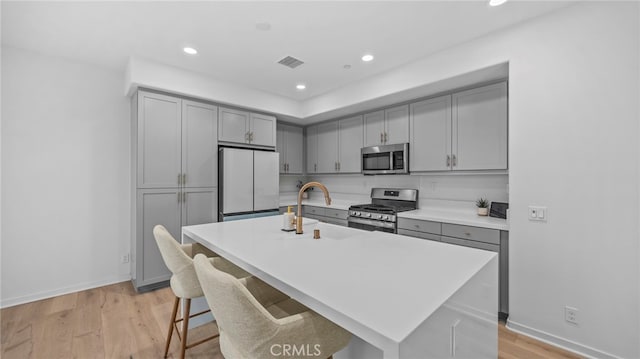 kitchen featuring sink, a center island with sink, stainless steel appliances, and light hardwood / wood-style floors