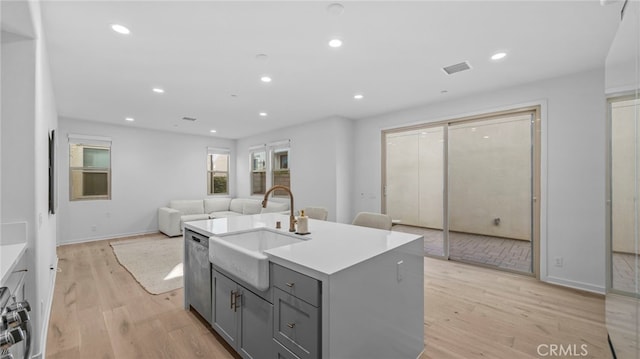 kitchen with sink, stainless steel dishwasher, gray cabinets, an island with sink, and light hardwood / wood-style floors