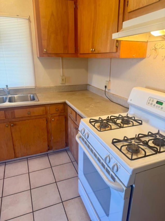 kitchen featuring white gas stove, light tile patterned floors, and sink