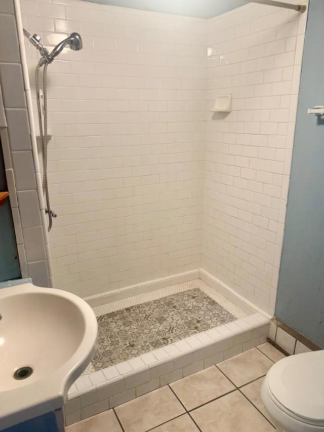 bathroom with tile patterned flooring, sink, toilet, and tiled shower