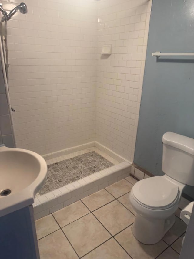 bathroom featuring tile patterned flooring, toilet, a tile shower, and vanity