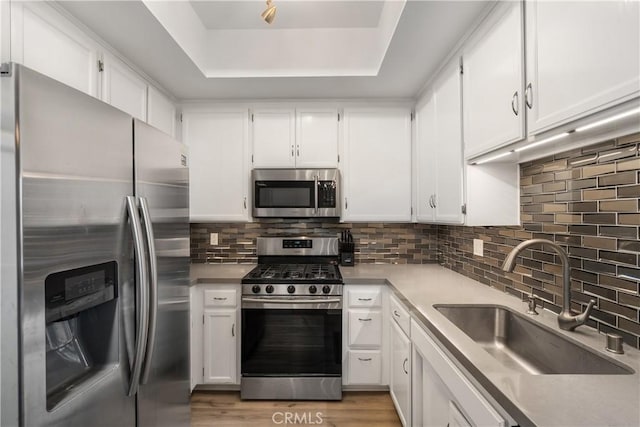 kitchen with sink, light wood-type flooring, appliances with stainless steel finishes, a tray ceiling, and white cabinetry