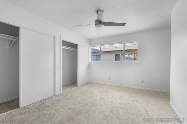 unfurnished bedroom with multiple closets, ceiling fan, and light carpet