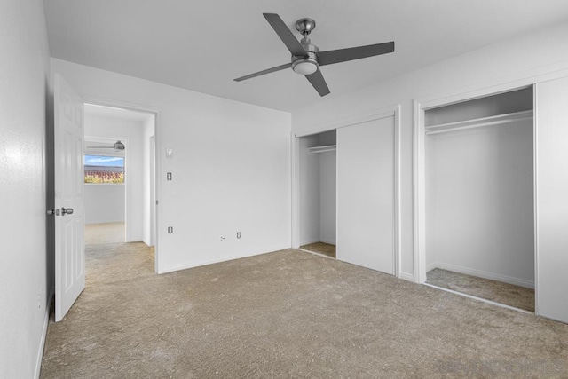 unfurnished bedroom featuring ceiling fan, light carpet, and two closets