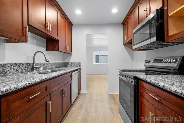 kitchen with appliances with stainless steel finishes, light hardwood / wood-style floors, light stone counters, and sink