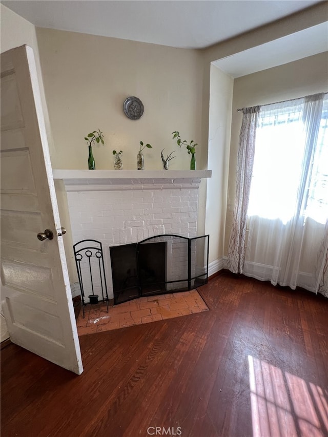 unfurnished living room featuring a brick fireplace and dark hardwood / wood-style flooring