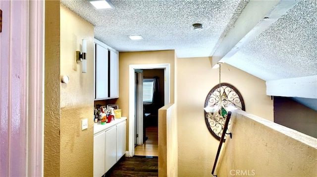 corridor with a textured ceiling, dark hardwood / wood-style flooring, and vaulted ceiling