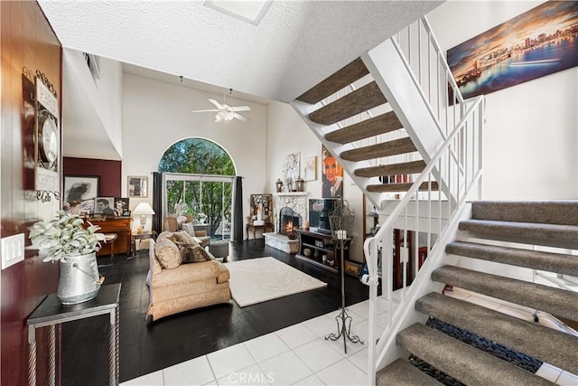 living room with ceiling fan, a stone fireplace, a textured ceiling, and high vaulted ceiling