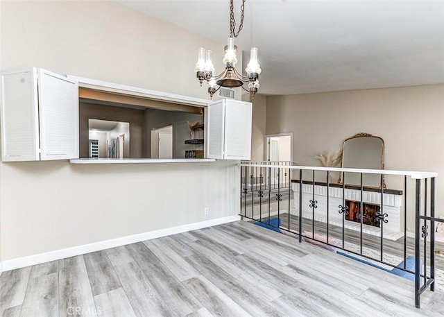 interior space featuring a brick fireplace, light hardwood / wood-style floors, and a chandelier