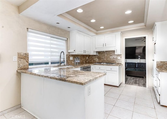 kitchen with kitchen peninsula, light stone counters, a tray ceiling, sink, and white cabinets