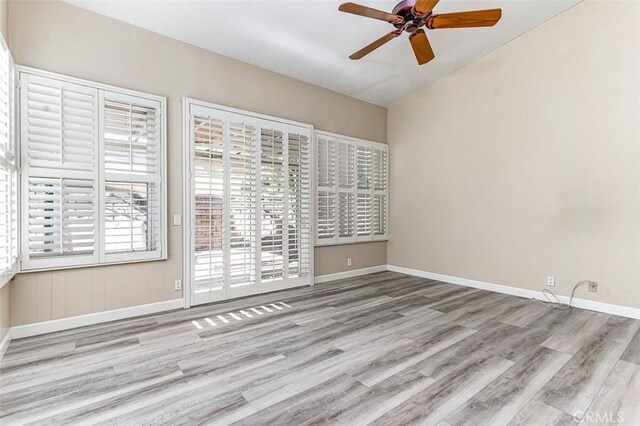 unfurnished room with lofted ceiling, light wood-type flooring, ceiling fan, and a healthy amount of sunlight