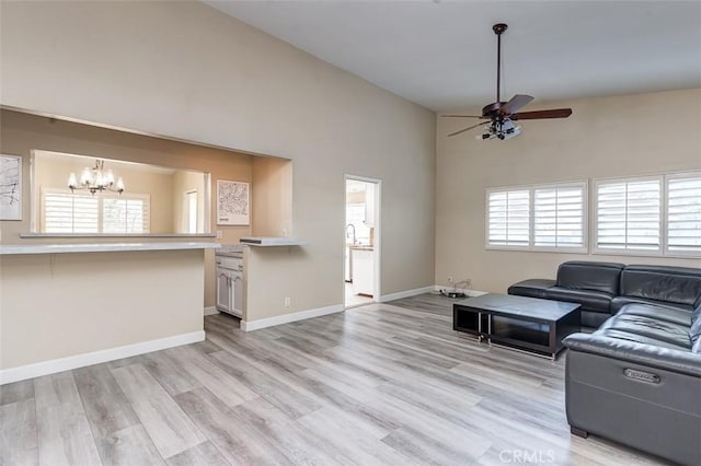 living room featuring high vaulted ceiling, ceiling fan with notable chandelier, and light wood-type flooring