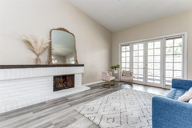 living area with a fireplace, french doors, wood-type flooring, and lofted ceiling