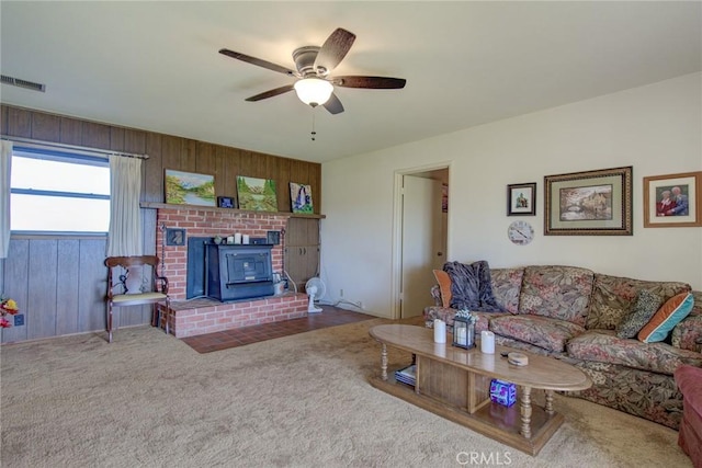 living room featuring carpet, ceiling fan, wood walls, and a wood stove