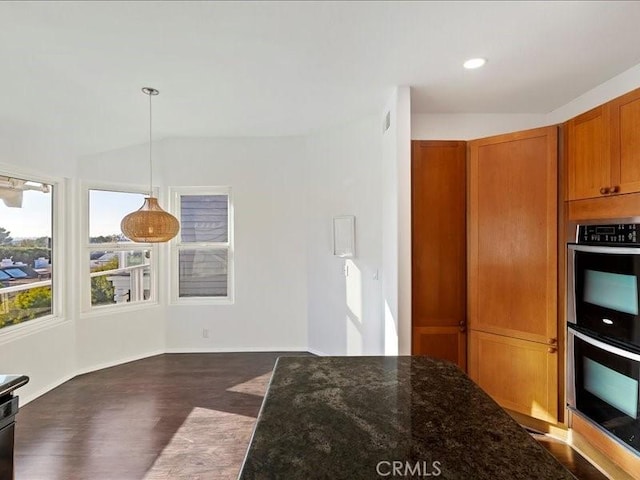 kitchen with dark stone counters, vaulted ceiling, double oven, dark wood-type flooring, and decorative light fixtures