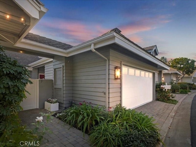 property exterior at dusk with decorative driveway and an attached garage