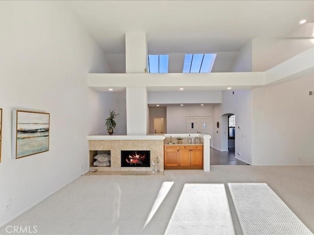 living room with a high ceiling, light carpet, a fireplace, arched walkways, and baseboards