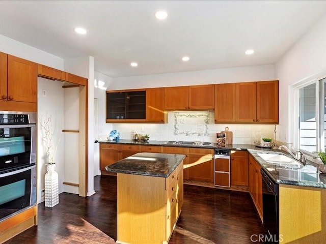 kitchen with a center island, sink, dark wood-type flooring, double oven, and dark stone counters