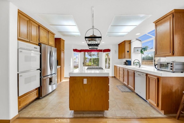 kitchen with white appliances, a kitchen island, decorative light fixtures, sink, and light tile patterned floors