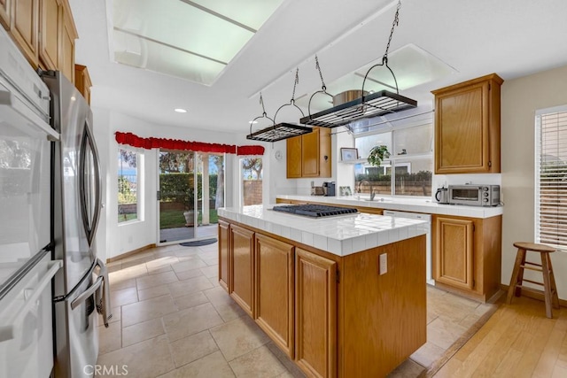 kitchen featuring dishwashing machine, a kitchen island, sink, tile countertops, and stainless steel refrigerator