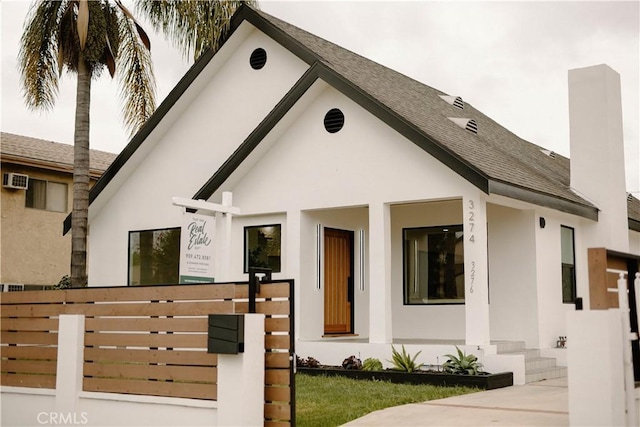view of front of house with stucco siding, fence, and a shingled roof