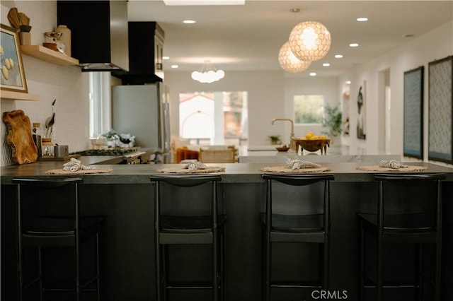 kitchen featuring recessed lighting, open shelves, freestanding refrigerator, decorative light fixtures, and a kitchen bar