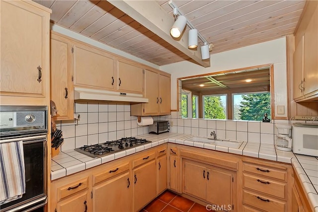 kitchen featuring tile countertops, black oven, sink, and stainless steel gas cooktop